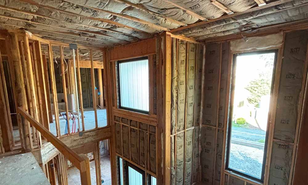 Choose Efficient Insulation for Your Project – Hudson Insulati Fiberglass batt insulation in walls and ceiling near an open stairway and window, single-family home in Brick, NJ, by Hudson Insulation.