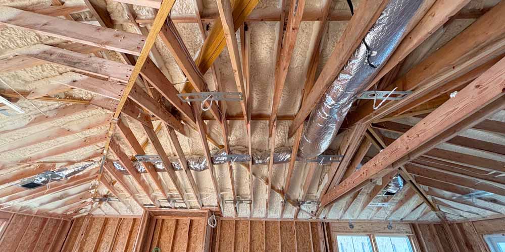 Open-cell spray foam insulation applied to roof rafters and ductwork in a vaulted attic space for a single-family home in Point Pleasant, NJ, by Hudson Insulation.
